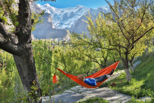 a red hammock set up between 2 trees with a person resting,