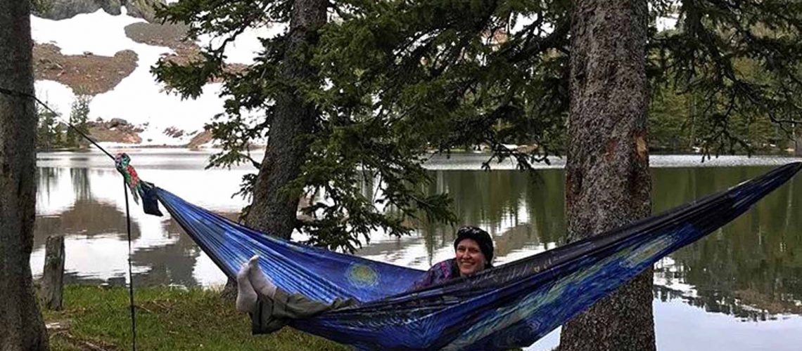 girl sitting and smiling in a blue hammock by a lake